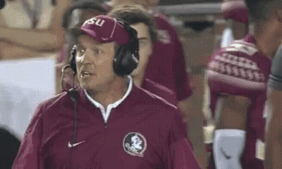 A Football Coach Wearing Headphones And A Hat Is Standing On The Sidelines . GIF