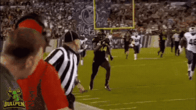 A Football Game Is Being Played On A Field With A Referee Standing In The Middle . GIF