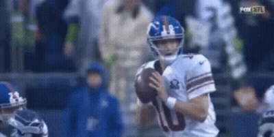 A Football Player For The New York Giants Is Holding A Football In His Hands . GIF