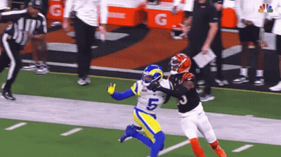A Football Player In A Blue And Yellow Uniform Is Trying To Catch A Pass From Another Player In A Black Uniform . GIF