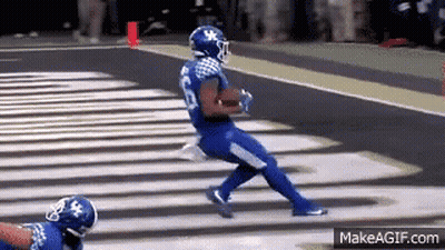 A Football Player In A Blue Jersey Is Running Down The Field . GIF
