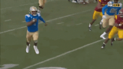 A Football Player In A Blue Jersey Is Running With A Ball On A Field . GIF