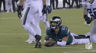 A Football Player In A Green Uniform Is Laying On The Field With A Ball . GIF