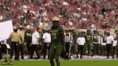A Football Player In A Green Uniform Is Walking On A Field With A Referee . GIF
