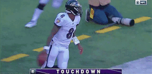 A Football Player In A Ravens Uniform Is Holding A Football In Front Of A Touchdown Screen GIF