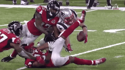 A Football Player Is Being Tackled By A Group Of Players On A Field . GIF