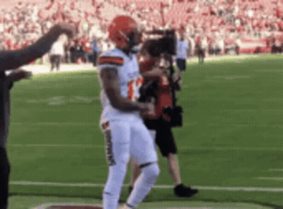 a football player is dancing on the field while a cameraman takes a picture .