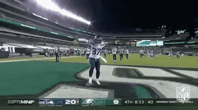 A Football Player Is Jumping In The Air On A Field During A Game GIF