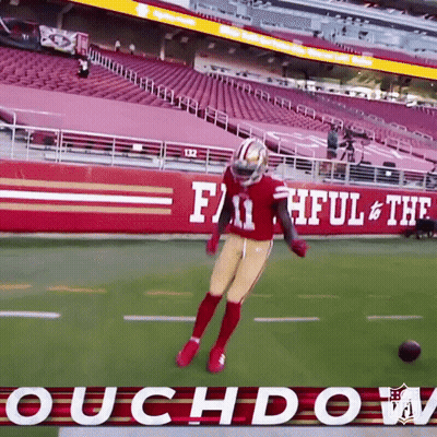 A Football Player Is Jumping In The Air On A Field In Front Of A Sign That Says Faithful & The Roughdown GIF