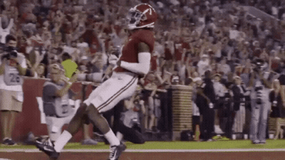 A Football Player Is Jumping In The Air While Catching A Pass On A Field . GIF