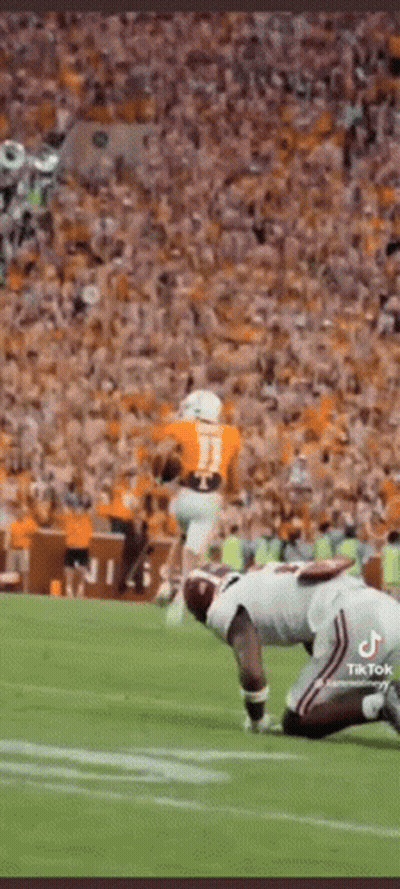 A Football Player Is Kneeling On The Field In Front Of A Crowd While Another Player Runs With The Ball . GIF