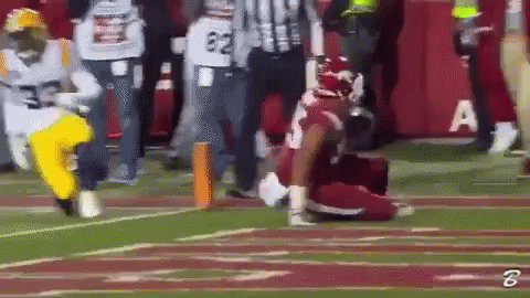 A Football Player Is Kneeling On The Field While A Referee Looks On GIF