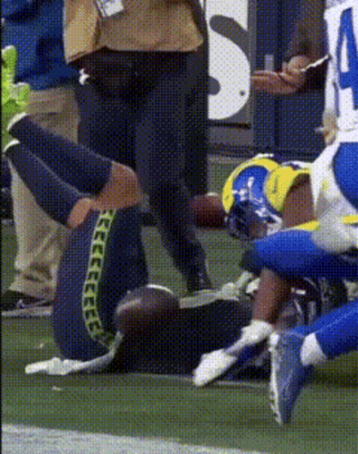 A Football Player Is Laying On The Field With His Knee Up GIF