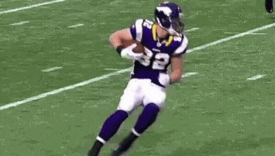 A Football Player Is Laying On The Ground While Another Player Tries To Tackle Him . GIF