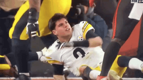 A Football Player Is Laying On The Ground While Being Helped By A Teammate . GIF
