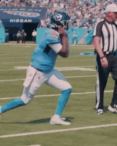 A Football Player Is Running On A Field With A Referee And A Nissan Sign In The Background GIF