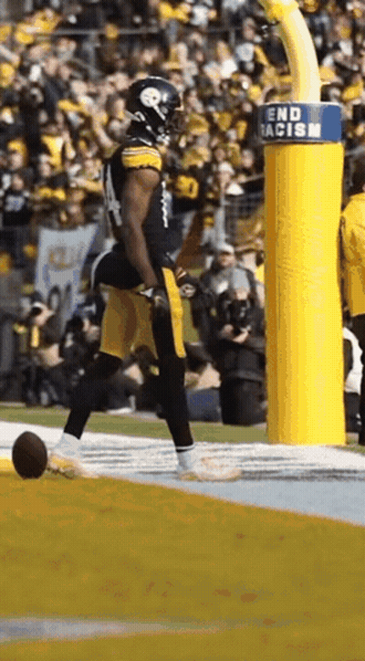 A Football Player Is Running On A Field With A Sign That Says End Racism . GIF
