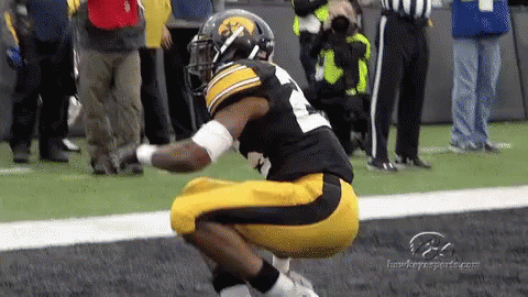 A Football Player Is Squatting Down On The Field While A Referee Looks On GIF