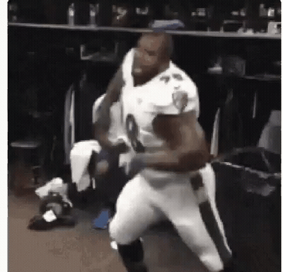 A Football Player Is Standing In A Locker Room With Another Player . GIF