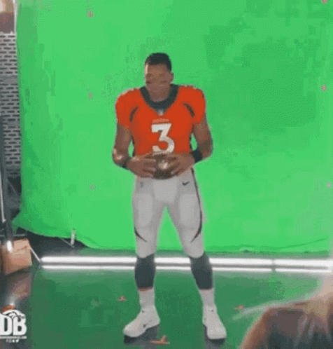 A Football Player Is Standing In Front Of A Green Screen And Holding A Football . GIF