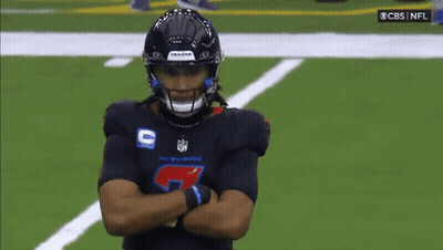A Football Player Is Standing On A Field With His Arms Crossed And A Referee Standing Behind Him . GIF