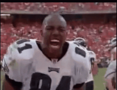 A Football Player Is Standing On A Field With His Mouth Open And A Crowd Behind Him . GIF