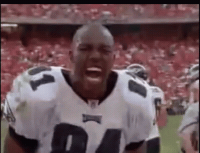 A Football Player Is Standing On A Field With His Mouth Open And A Crowd Behind Him . GIF