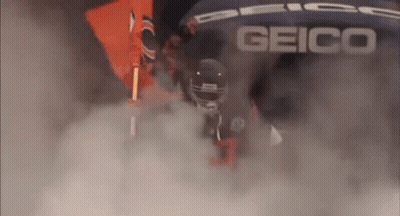 A Football Player Is Walking Through A Cloud Of Smoke While Wearing A Helmet . GIF
