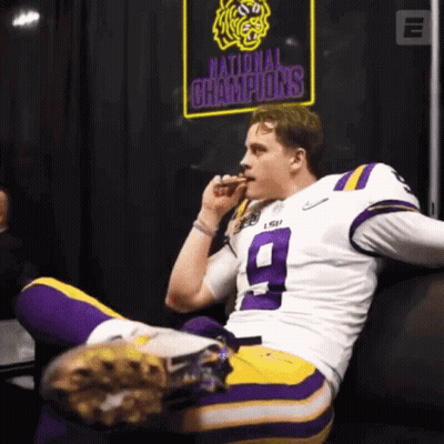 A Football Player Sitting On A Couch With A National Champions Sign Behind Him GIF