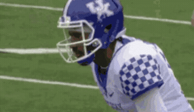 A Football Player Wearing A Blue Helmet And A Checkered Jersey Is Standing On The Field . GIF