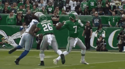 A Football Player Wearing A Green Jersey With The Number 7 On It Is Being Tackled By Another Player . GIF
