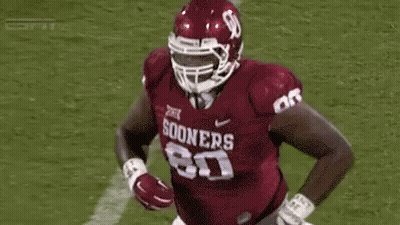 A Football Player Wearing A Helmet And A Maroon Jersey Is Running On The Field . GIF