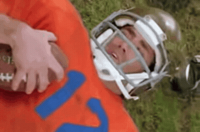 A Football Player Wearing A Helmet Is Laying On The Grass With A Football . GIF