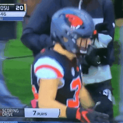 A Football Player Wearing A Helmet Is Sitting On A Field With A Scoreboard That Says Scoring Drive GIF
