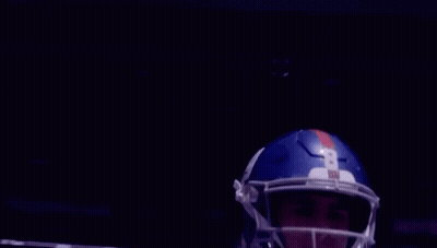 A Football Player Wearing A Helmet Is Standing In Front Of A Stadium . GIF