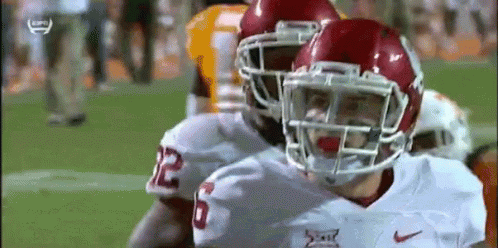 A Football Player Wearing A Helmet Is Standing Next To Another Player On The Field . GIF