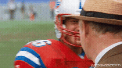 A Football Player Wearing A Helmet Is Talking To A Man Wearing A Hat On A Field . GIF