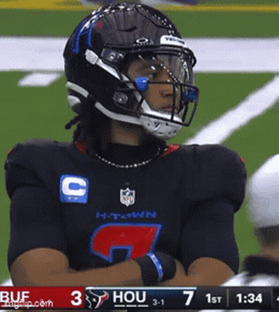 A Football Player Wearing A Helmet Stands On A Field With His Arms Crossed GIF