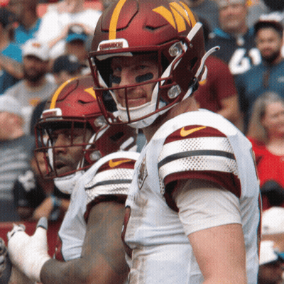A Football Player Wearing A Helmet That Says Washington Stands Next To Another Player GIF
