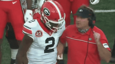 A Football Player Wearing A Helmet With The Number 2 On It Is Running On The Field While A Coach Watches . GIF