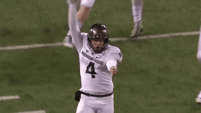 A Football Player Wearing A Michigan State Jersey Is Kicking A Ball On The Field . GIF