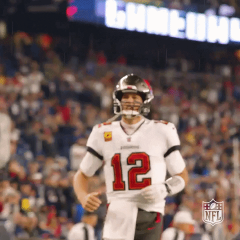 A Football Player Wearing A Number 12 Jersey Is Running On The Field . GIF