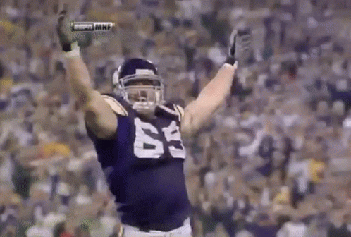 A Football Player Wearing A Purple Jersey With The Number 63 On It Is Standing On A Field With His Arms In The Air . GIF
