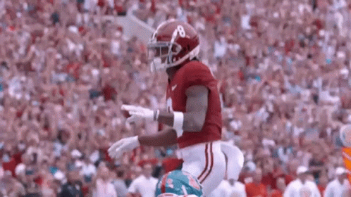 A Football Player Wearing A Red Helmet And White Pants Is Running On A Field . GIF