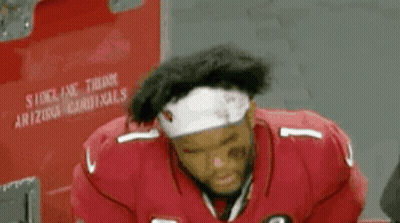 A Football Player Wearing A Red Jersey And A White Headband Is Sitting In A Locker Room . GIF