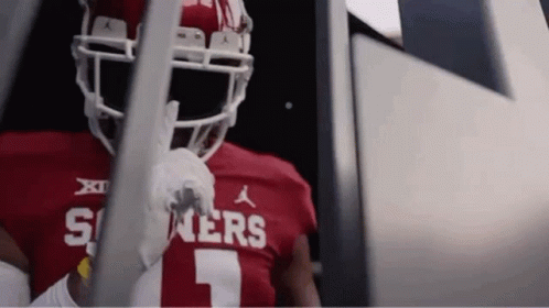 A Football Player Wearing A Red Jersey And White Helmet Is Standing In A Locker Room . GIF