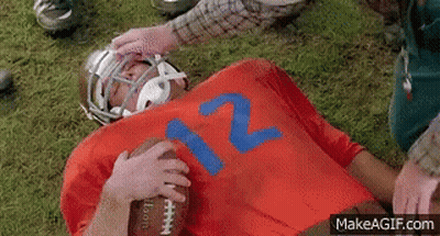 A Football Player Wearing A Red Jersey With The Number 12 On It Is Laying On The Ground . GIF
