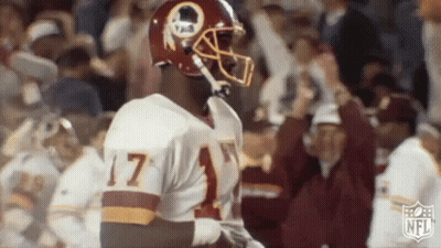 A Football Player Wearing A Redskins Uniform And Helmet Is Standing In Front Of A Crowd . GIF