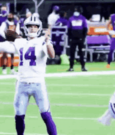 A Football Player Wearing A White And Purple Uniform Is Standing On A Field . GIF