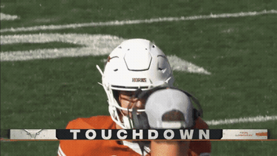 A Football Player Wearing Headphones And A White Helmet Stands In Front Of A Banner That Says Touchdown On It GIF